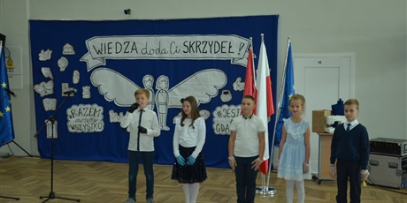 Powiększ grafikę: grupa dzieci ubranych galowo ma tle dekoracji pt."Wiedza doda Ci skrzydeł"