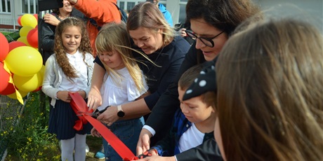 Powiększ grafikę: prezydent Dulkiewicz w towarzystwie kierowniczki administracyjnej przecina wstęgę otwierając szkolny plac zabaw