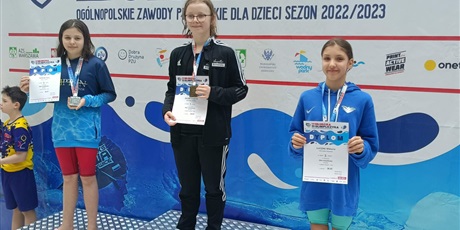 Powiększ grafikę: trzy dziewczynki na podium po zawodach pływackich na basenie