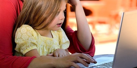 Powiększ grafikę: zdjęcie - dziewczynka siędząca na kolanach u rodzica prze ekranem komputera