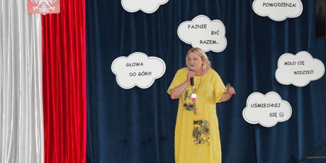Powiększ grafikę: pani dyrektor Katarzyna Kędzioł na tle dekoracji (białe chmurki na granatowym tle) przemawia do zebranych