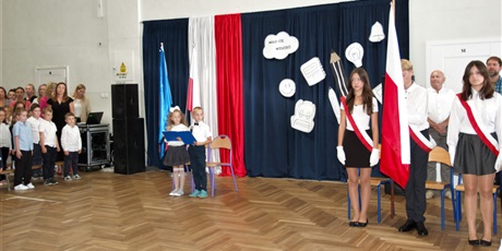 Powiększ grafikę: chłopiec i dziewczynka z klas młodszych oraz poczet flagowy na tle dekoracji